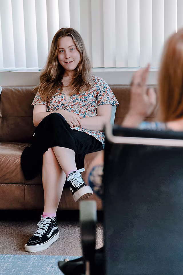 Young woman client sitting on couch listening to therapist.
