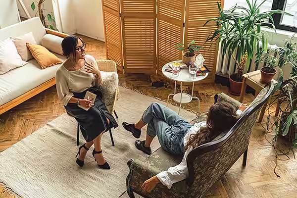 Therapist office with natural colors and lighting. Therapist in chair facing and talking to client.